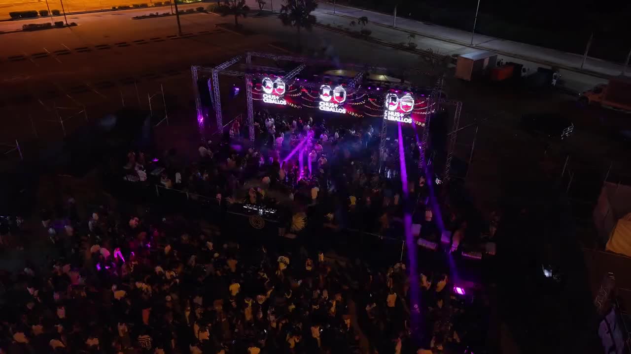 Toma aérea nocturna de un evento con escenario y público